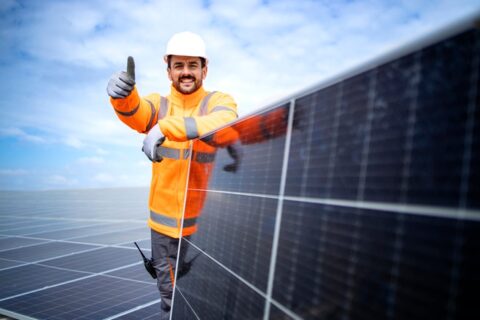 Portrait of professional worker standing by solar panel and holding thumbs up.